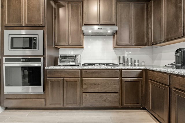 kitchen with a toaster, under cabinet range hood, dark brown cabinets, appliances with stainless steel finishes, and decorative backsplash