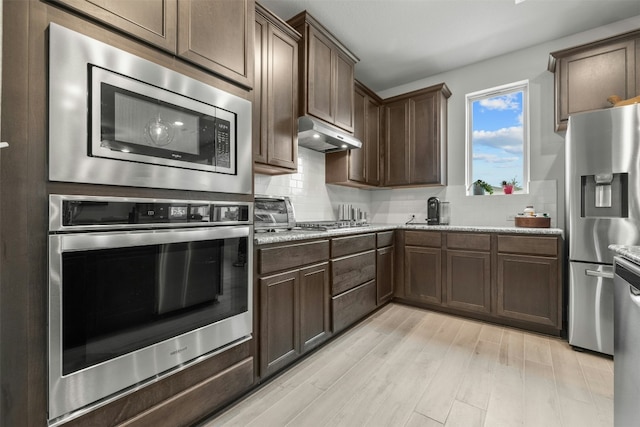 kitchen with appliances with stainless steel finishes, under cabinet range hood, light wood finished floors, and tasteful backsplash