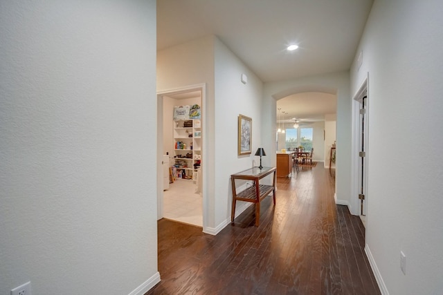 hall featuring baseboards, arched walkways, dark wood-style flooring, and recessed lighting