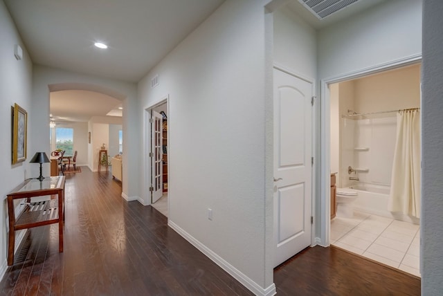 corridor with baseboards, visible vents, arched walkways, and wood finished floors