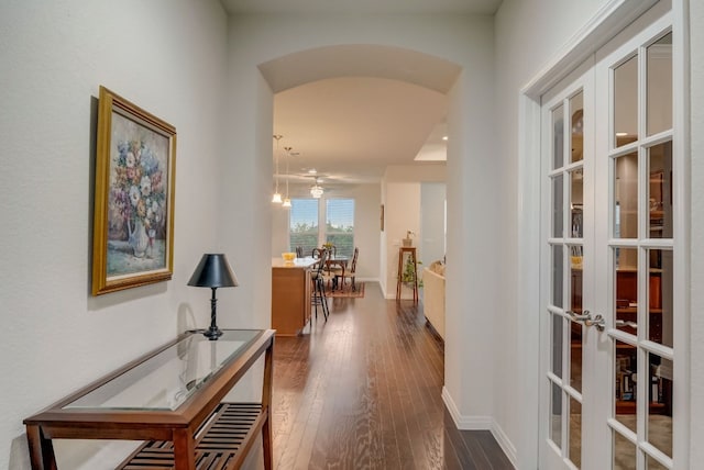 hallway featuring arched walkways, dark wood finished floors, and baseboards