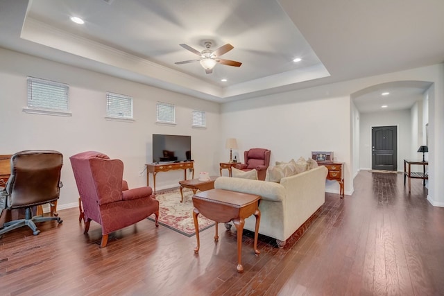 living area featuring baseboards, a tray ceiling, arched walkways, and dark wood-type flooring