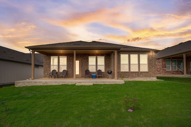 back of house with brick siding, a yard, and a patio