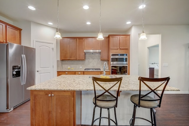 kitchen with under cabinet range hood, dark wood finished floors, stainless steel appliances, and a sink