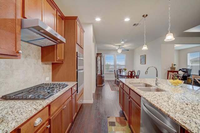 kitchen featuring appliances with stainless steel finishes, brown cabinets, dark wood-type flooring, range hood, and a sink