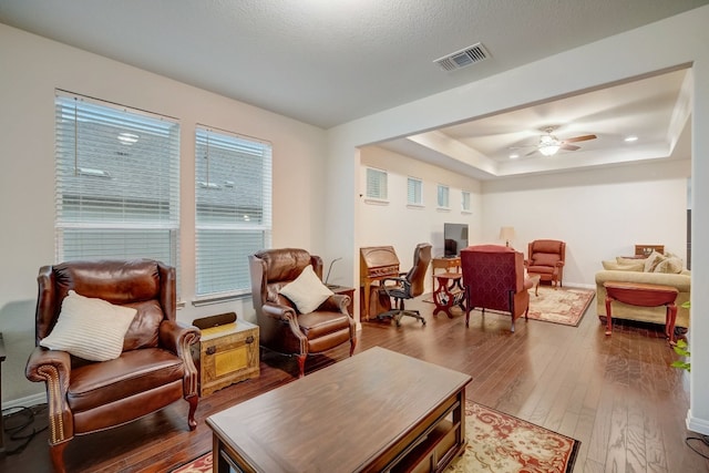 living area featuring baseboards, visible vents, a ceiling fan, a raised ceiling, and hardwood / wood-style floors