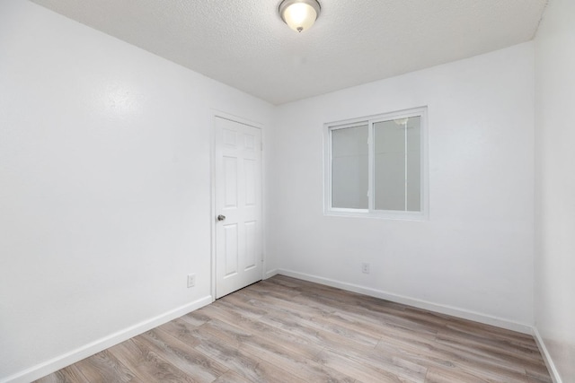 unfurnished room with light wood-style flooring, baseboards, and a textured ceiling