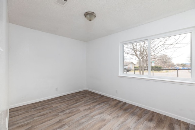 empty room with visible vents, baseboards, a textured ceiling, and light wood finished floors