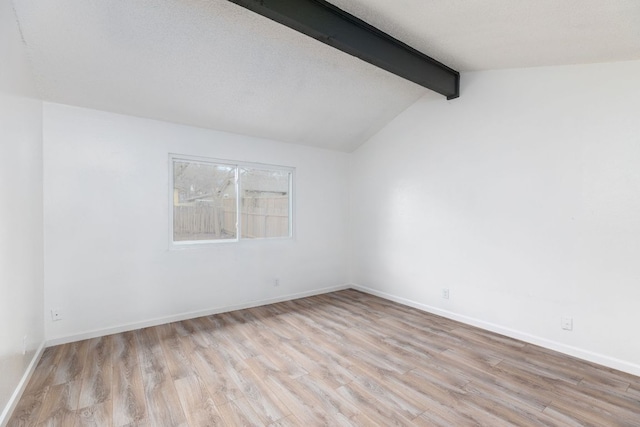 empty room featuring lofted ceiling with beams, a textured ceiling, baseboards, and wood finished floors