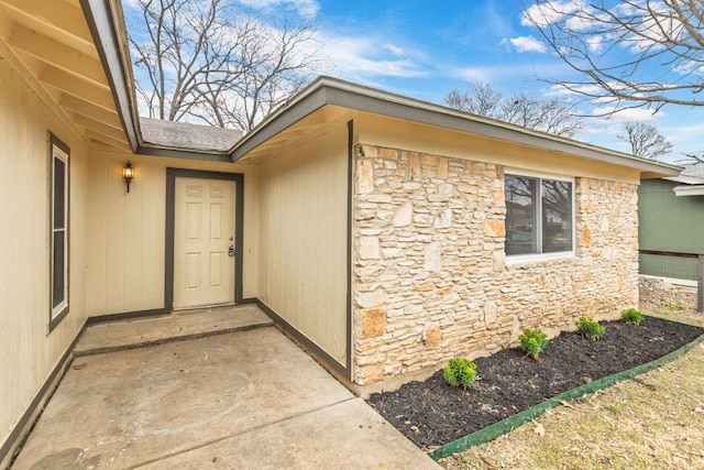 view of exterior entry with stone siding and roof with shingles