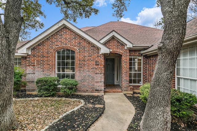 ranch-style house featuring a shingled roof and brick siding