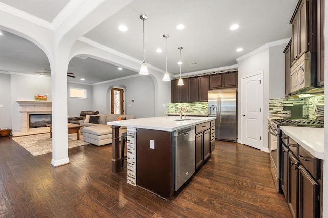 kitchen with arched walkways, stainless steel appliances, a glass covered fireplace, open floor plan, and dark brown cabinets