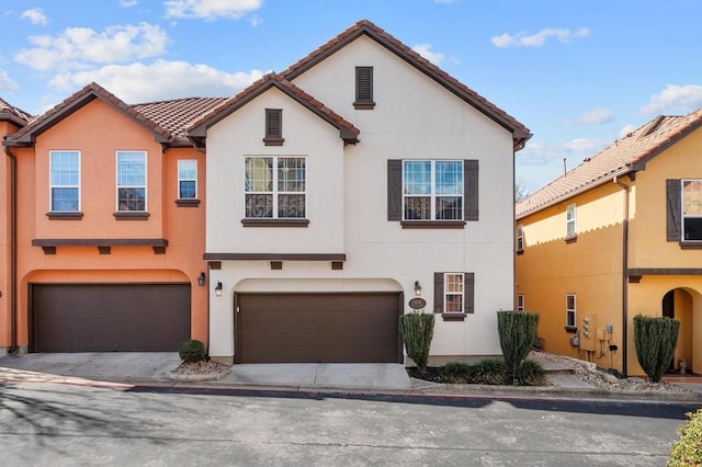 view of property featuring a tiled roof, a garage, and stucco siding
