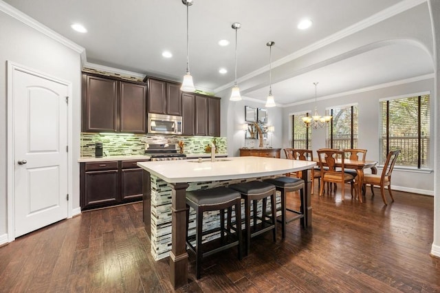 kitchen with tasteful backsplash, dark wood-style floors, appliances with stainless steel finishes, a kitchen breakfast bar, and light countertops