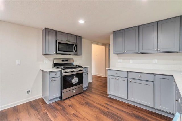 kitchen with baseboards, appliances with stainless steel finishes, dark wood-style flooring, light countertops, and gray cabinetry