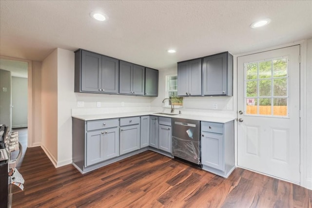 kitchen featuring dark wood-style flooring, light countertops, gray cabinetry, stainless steel dishwasher, and a sink