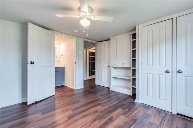 unfurnished bedroom featuring multiple closets, dark wood finished floors, baseboards, and ceiling fan