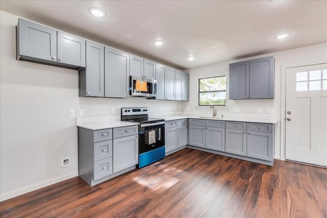 kitchen featuring dark wood-style flooring, light countertops, gray cabinetry, appliances with stainless steel finishes, and a sink