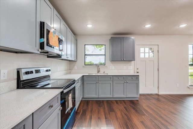 kitchen featuring stainless steel appliances, a sink, a healthy amount of sunlight, gray cabinets, and dark wood-style floors