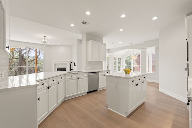 kitchen with a peninsula, a sink, visible vents, stainless steel dishwasher, and light wood finished floors