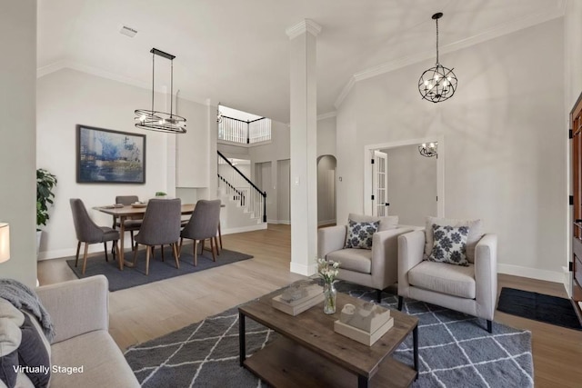 living area with ornamental molding, a chandelier, a towering ceiling, and wood finished floors