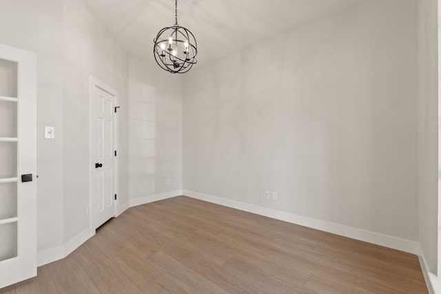 unfurnished room with an inviting chandelier, built in shelves, baseboards, and wood finished floors