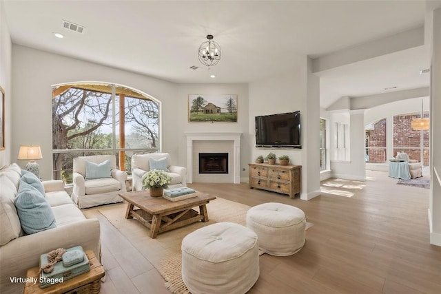 living room featuring a chandelier, light wood-style floors, visible vents, and a fireplace