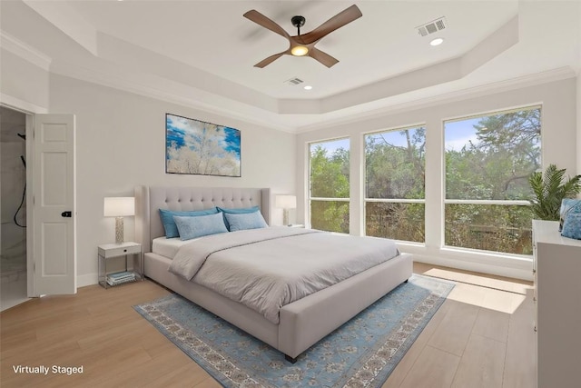 bedroom with light wood-type flooring, visible vents, a raised ceiling, and ornamental molding