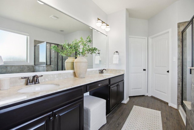 full bath with double vanity, wood finished floors, a sink, and a shower stall