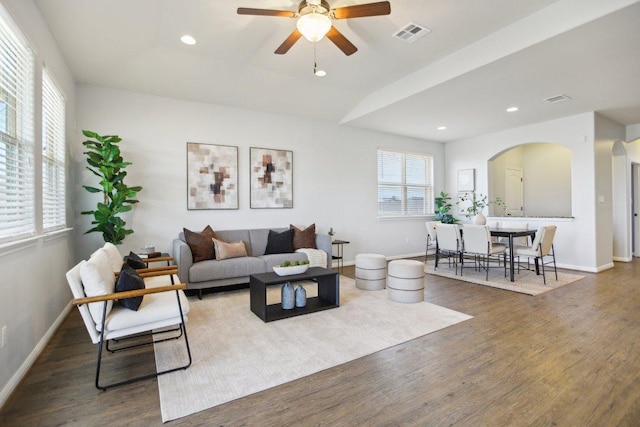 living room with arched walkways, visible vents, baseboards, and wood finished floors