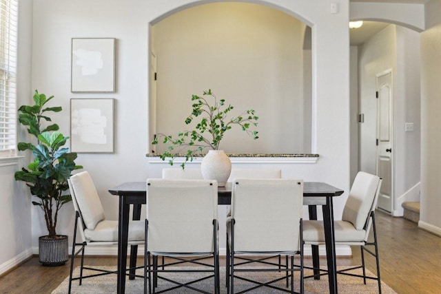 dining room featuring arched walkways, wood finished floors, a wealth of natural light, and baseboards