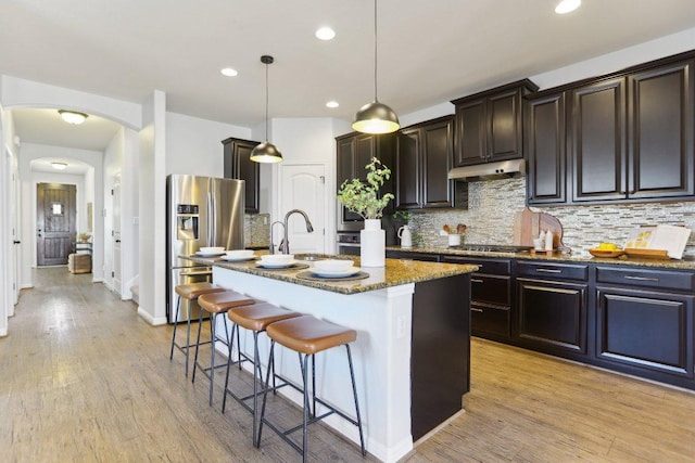 kitchen featuring arched walkways, a breakfast bar, a sink, appliances with stainless steel finishes, and dark stone countertops