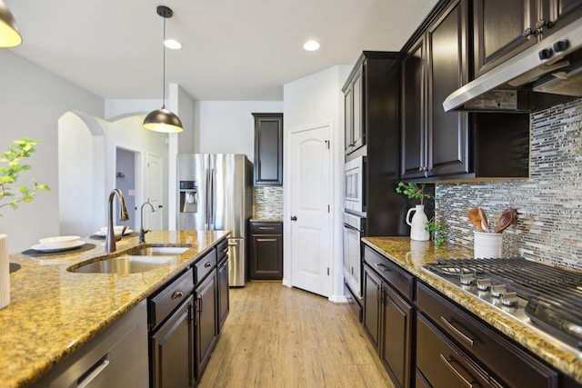 kitchen featuring arched walkways, stainless steel appliances, a sink, light stone countertops, and under cabinet range hood