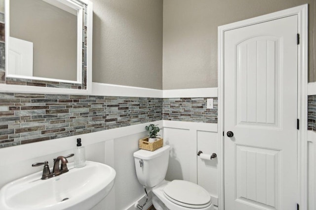 bathroom featuring toilet, tile walls, a sink, and wainscoting