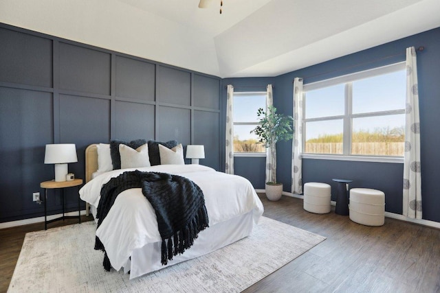 bedroom featuring lofted ceiling, wood finished floors, and a decorative wall