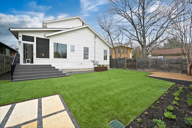 back of property with a sunroom, a lawn, a fenced backyard, and entry steps