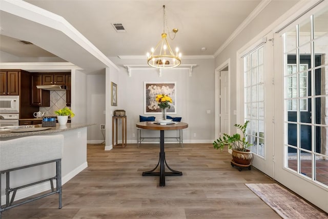 dining room with a notable chandelier, visible vents, baseboards, light wood-style floors, and ornamental molding