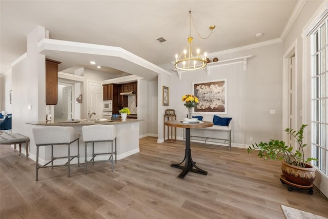 kitchen featuring white microwave, light wood-type flooring, a kitchen bar, and a notable chandelier