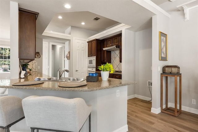 kitchen with light wood-style flooring, under cabinet range hood, white appliances, a sink, and visible vents