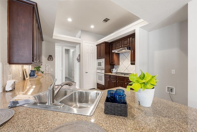 kitchen featuring under cabinet range hood, white appliances, a sink, visible vents, and decorative backsplash