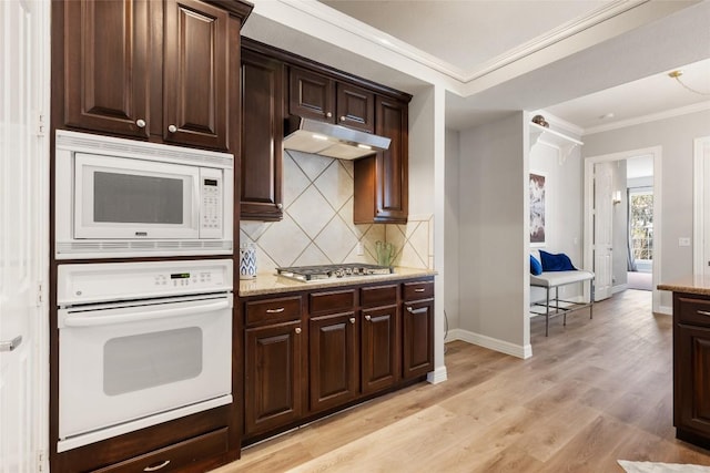 kitchen featuring under cabinet range hood, white appliances, ornamental molding, decorative backsplash, and light wood finished floors