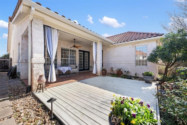 rear view of property with stucco siding, a tile roof, a ceiling fan, and a wooden deck