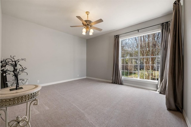 carpeted spare room featuring baseboards and a ceiling fan