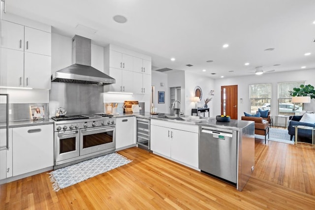 kitchen with wine cooler, a peninsula, stainless steel appliances, white cabinets, and wall chimney exhaust hood