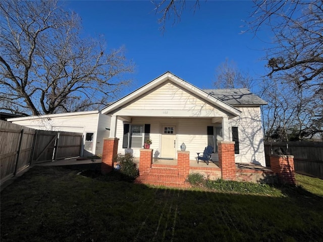 rear view of property featuring covered porch, a lawn, and fence