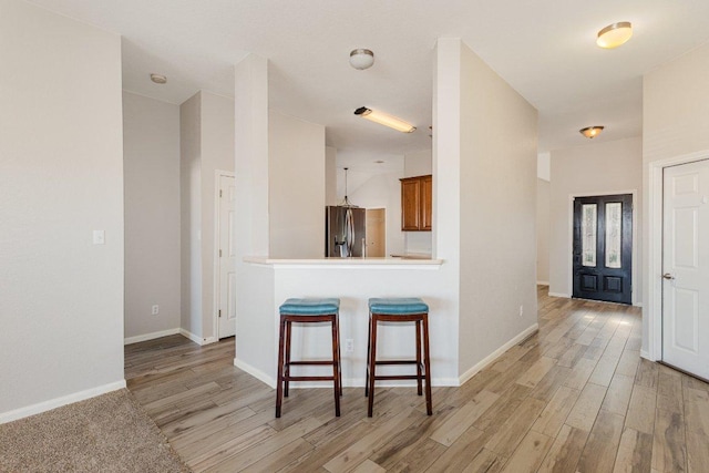 kitchen featuring light wood-style floors, brown cabinets, stainless steel fridge, and a breakfast bar area