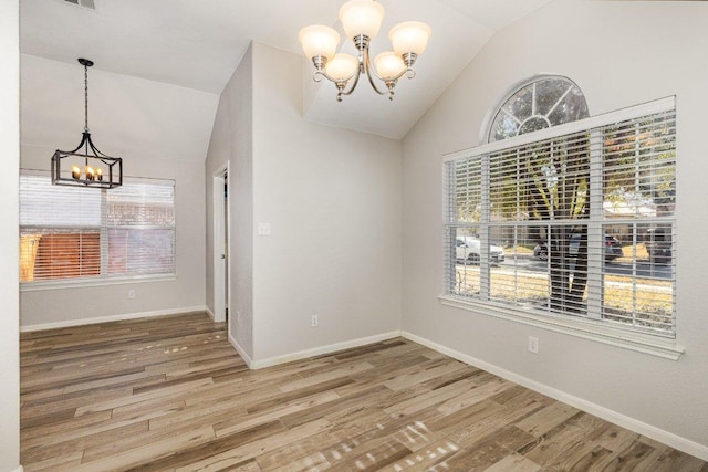 unfurnished dining area with wood finished floors, vaulted ceiling, baseboards, and an inviting chandelier