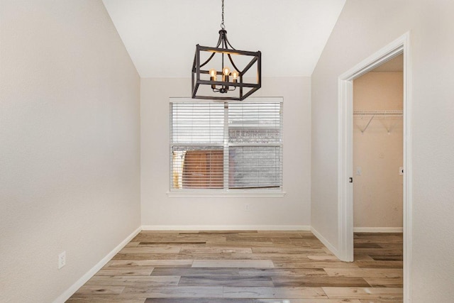 unfurnished dining area with vaulted ceiling, baseboards, wood finished floors, and a notable chandelier