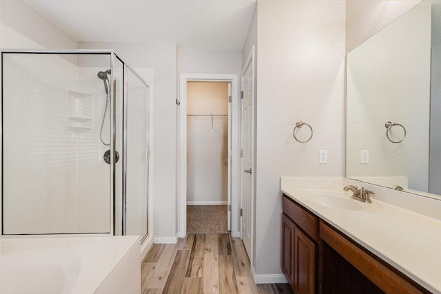 bathroom with a stall shower, a walk in closet, vanity, and wood finished floors