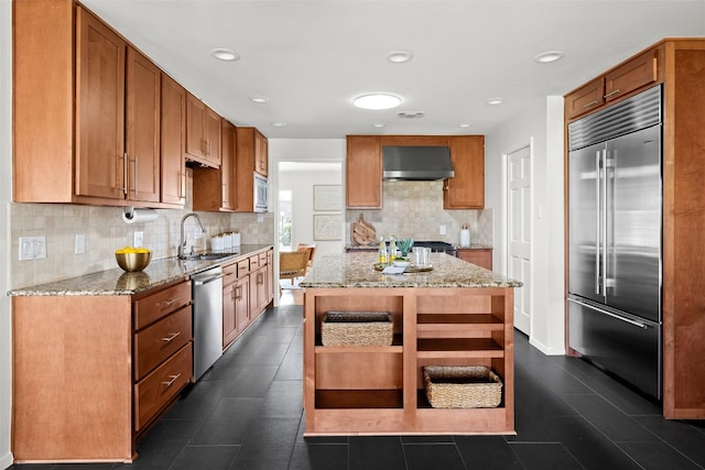 kitchen featuring tasteful backsplash, light stone counters, built in appliances, a sink, and exhaust hood